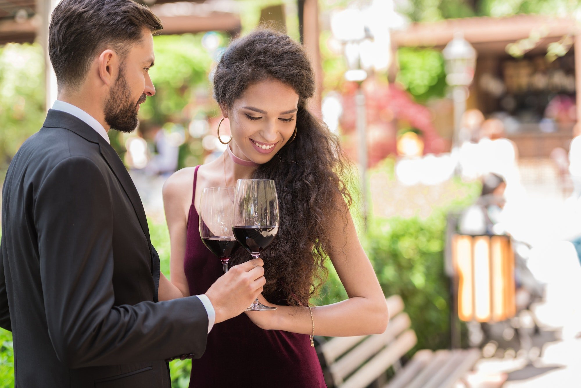 Couple having romantic date, standing in garden and clinking glasses